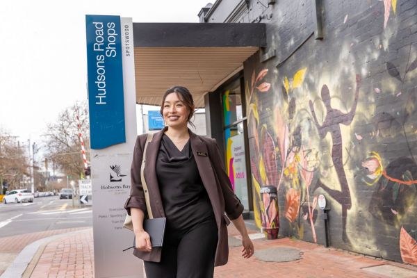 Dr Jenny Dang walks along the street in Spotswood. Behind her is a sign saying ‘Hudsons Road Shops’