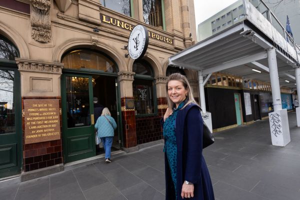 Associate Professor Rita Hardiman stands on the pavement outside the Young & Jackson pub and near a white hoarding concealing the Metro Rail Tunnel construction site in the Melbourne CBD.