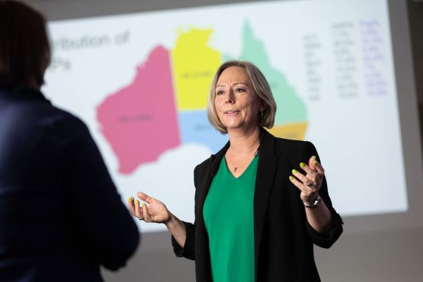 Alum Associate Professor Roisin McGrath speaks to someone off-camera while standing in front of a colourful map of Australia