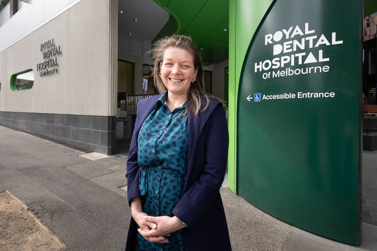 Associate Professor Rita Hardiman smiles at the camera as she stands in front of the entrance to the Royal Dental Hospital of Melbourne