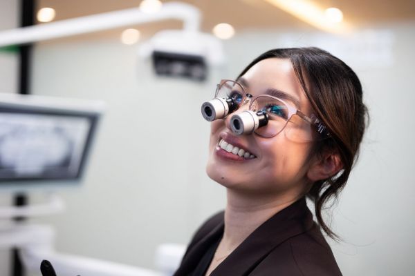 Headshot of Alum Dr Jenny Dang, who is smiling, wearing dental loupes