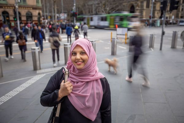 Dr Nadia Kaunein in the foreground smiling with people crossing at the pedestrian lights in the lights in the background