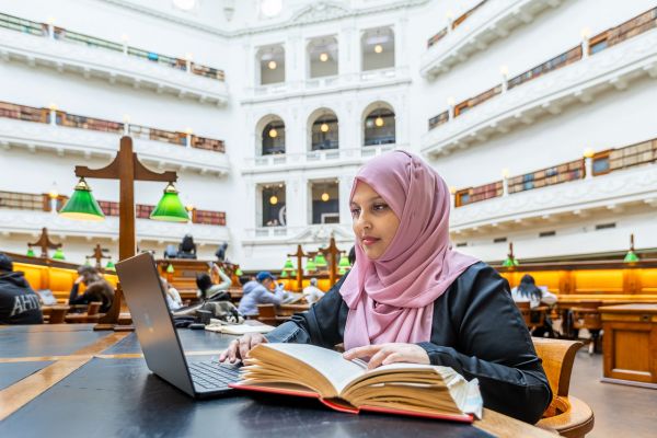 Dr Nadia Kaunein sitting at a desk and looking at a laptop in the reading room of the State Library of Victoria