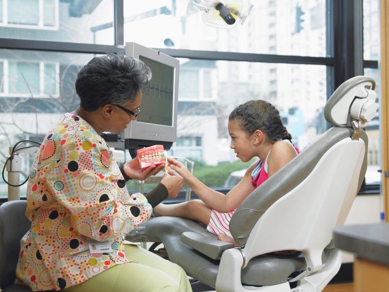 A young girl being taught to brush her teeth by a dentist